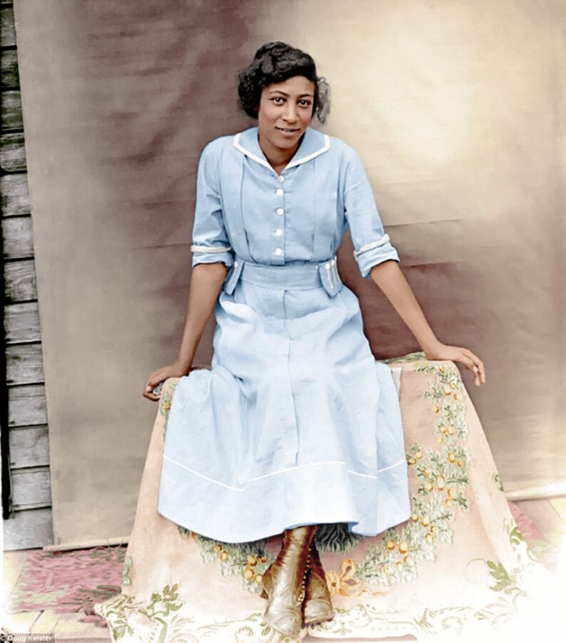 This is a colorized photo of the previous image. The young woman's dress is now blue, and the shawl draped over the box on which she sits is peach with a green wreath.
