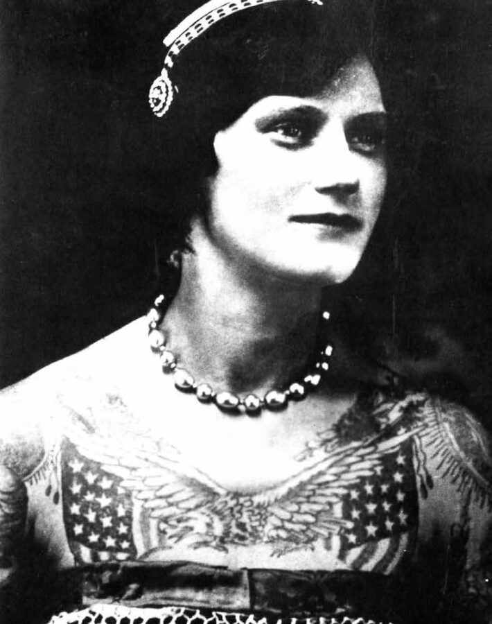 A young white woman has a large tattoo on her chest of an eagle, flanked by two American flags.