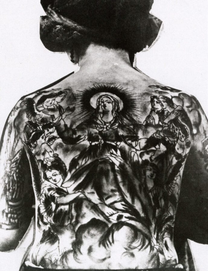 A woman has a large backpiece with the Virgin Mary at its center. Angels flank the Virgin Mary.