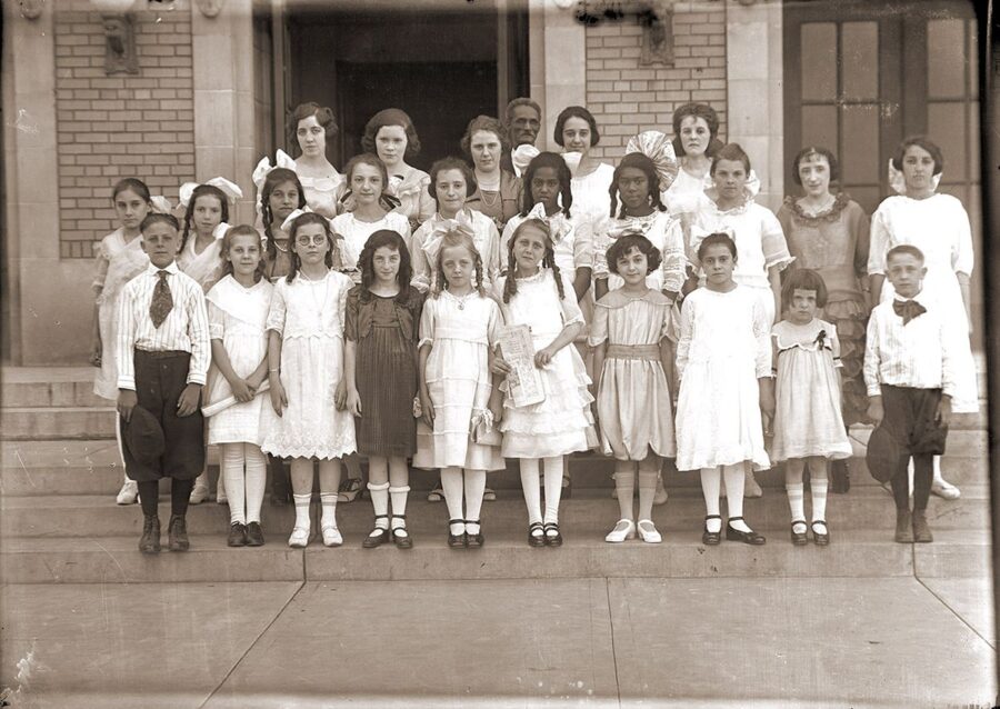 A group of children and adults stand in front of a brick building. They are all posed for a portrait and looking straight ahead.